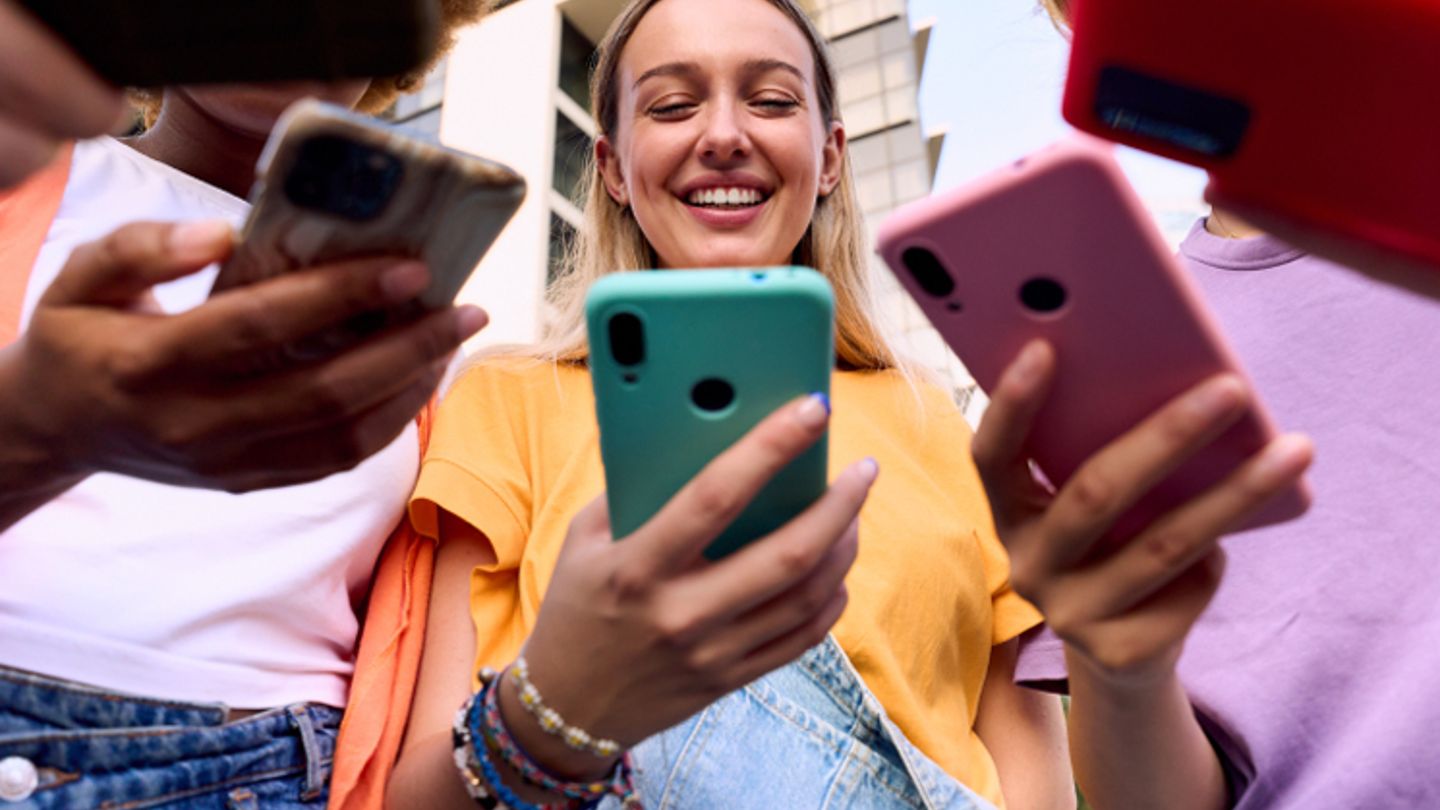 Group of young friends outdoors, smiling and engaging with their smartphones in a modern urban setting