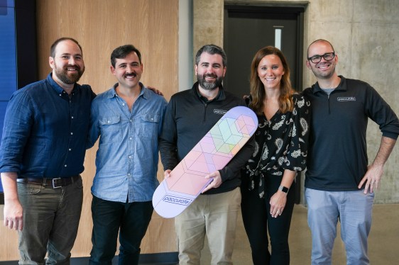 Image of five Paccurate team members with co-founder and CEO James Malley in the middle holding a skateboard that says Paccurate