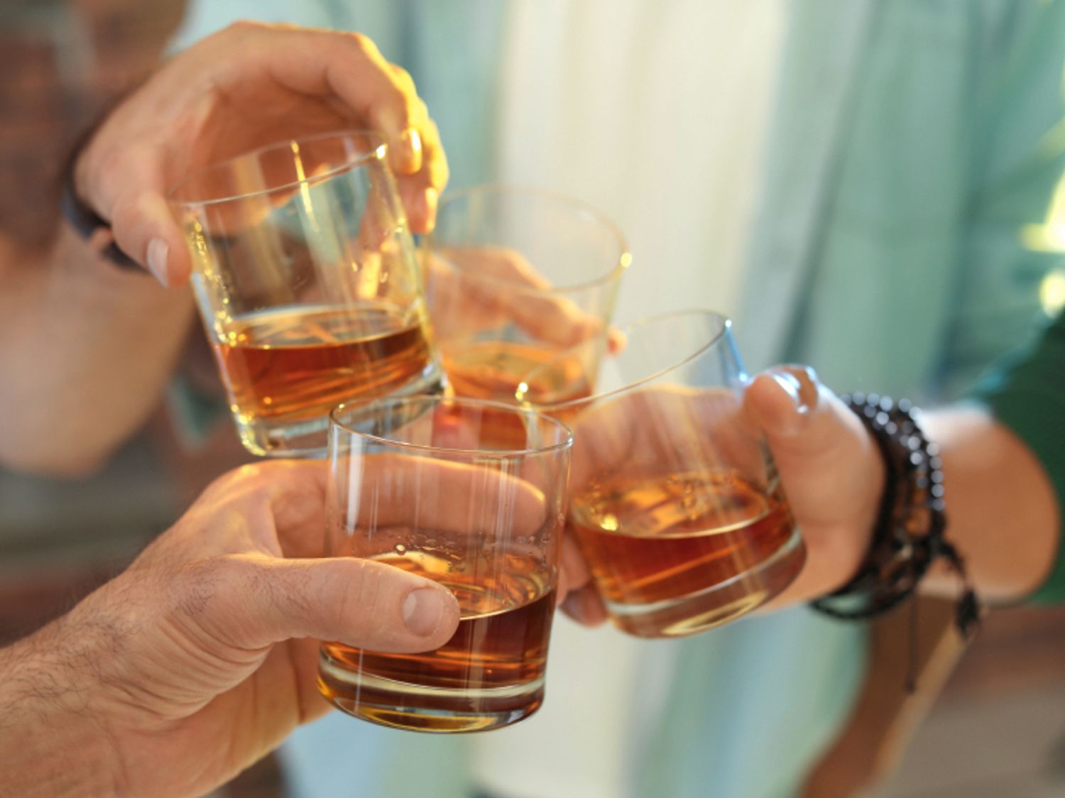 Five hands clink glasses filled with whiskey, in a celebratory toast. Five hands clink glasses filled with whiskey, in a celebratory toast.