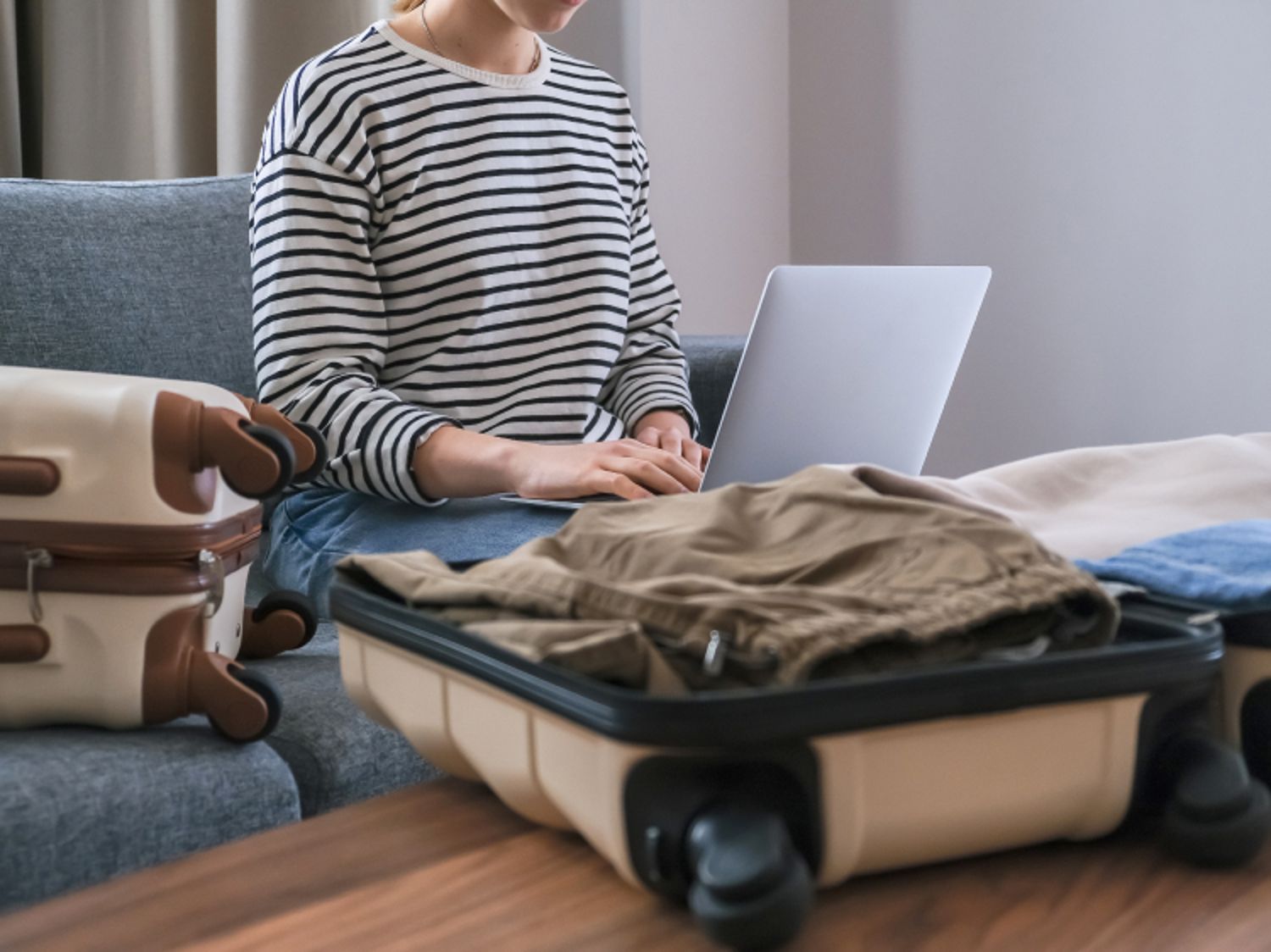 Woman typing on a laptop with two suitcase open, while packing.