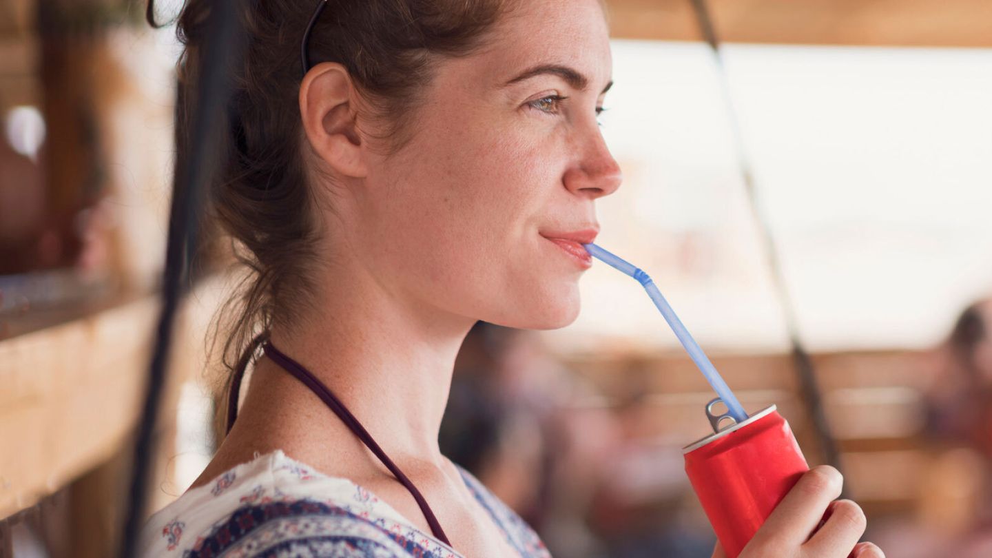 Woman standing and drinking out a red can from a blue straw