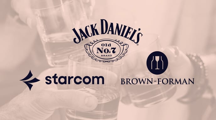 Five hands clink glasses filled with whiskey, in a celebratory toast with warm peach overlay and Jack Daniel's + Starcom + Brown-Forman logo over top.